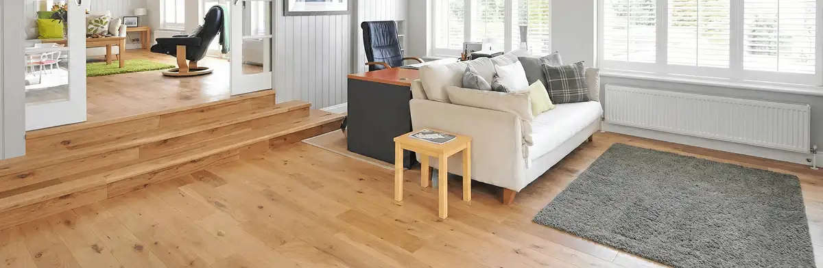 A modern living room with professionally installed laminate flooring, a beige sofa, a small side table, a gray rug, and large windows with white shutters in Aurora, IL